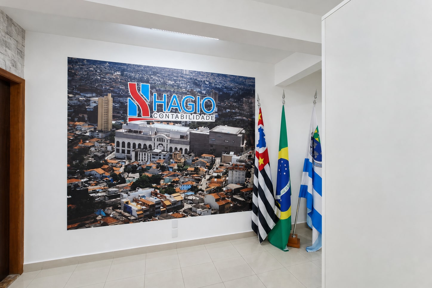 Recepção do escritório, com um painel na parede trazendo o logotipo da Hagio Contabilidade e três bandeiras ao lado.